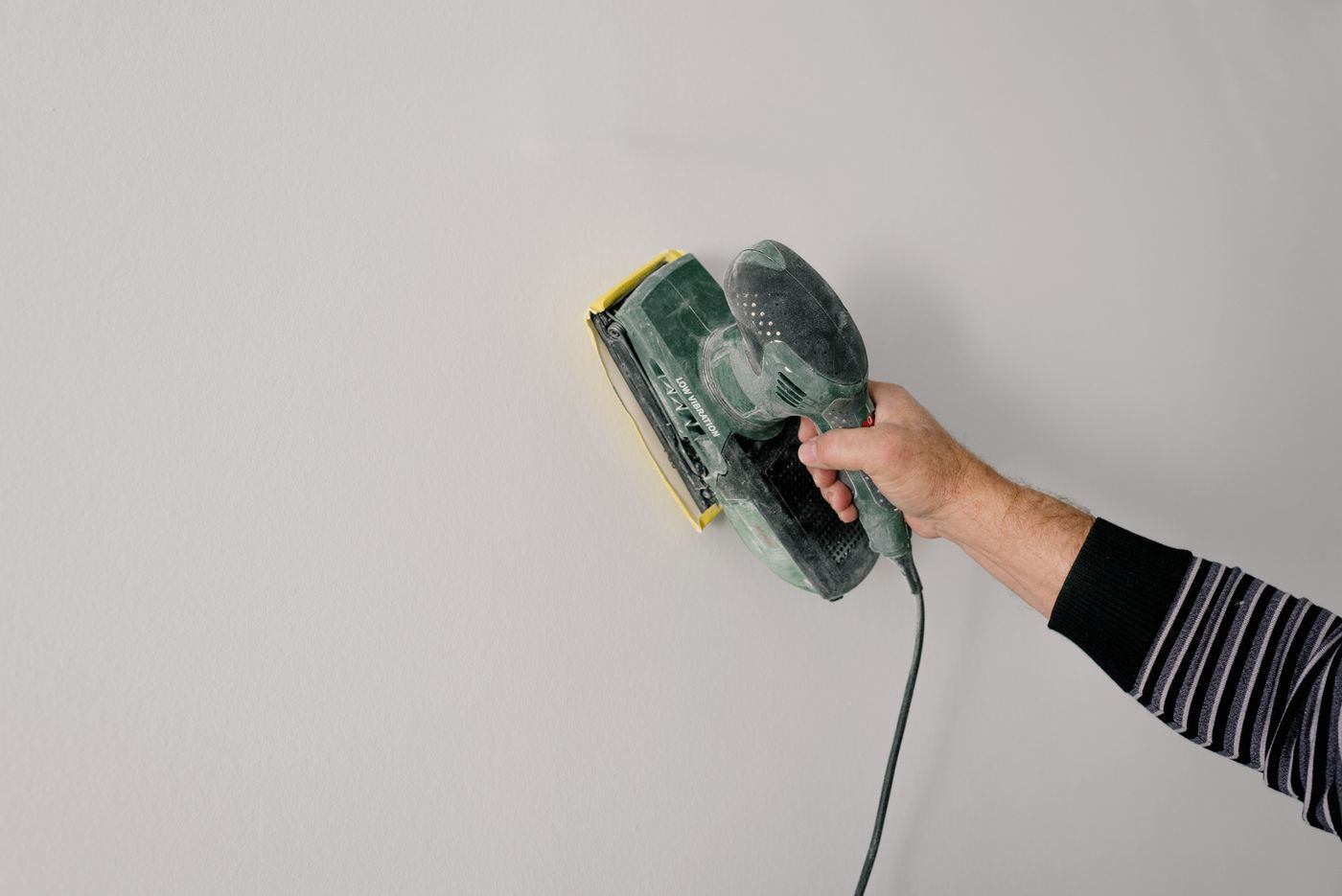 Hand schuurt een witte muur met een schuurmachine